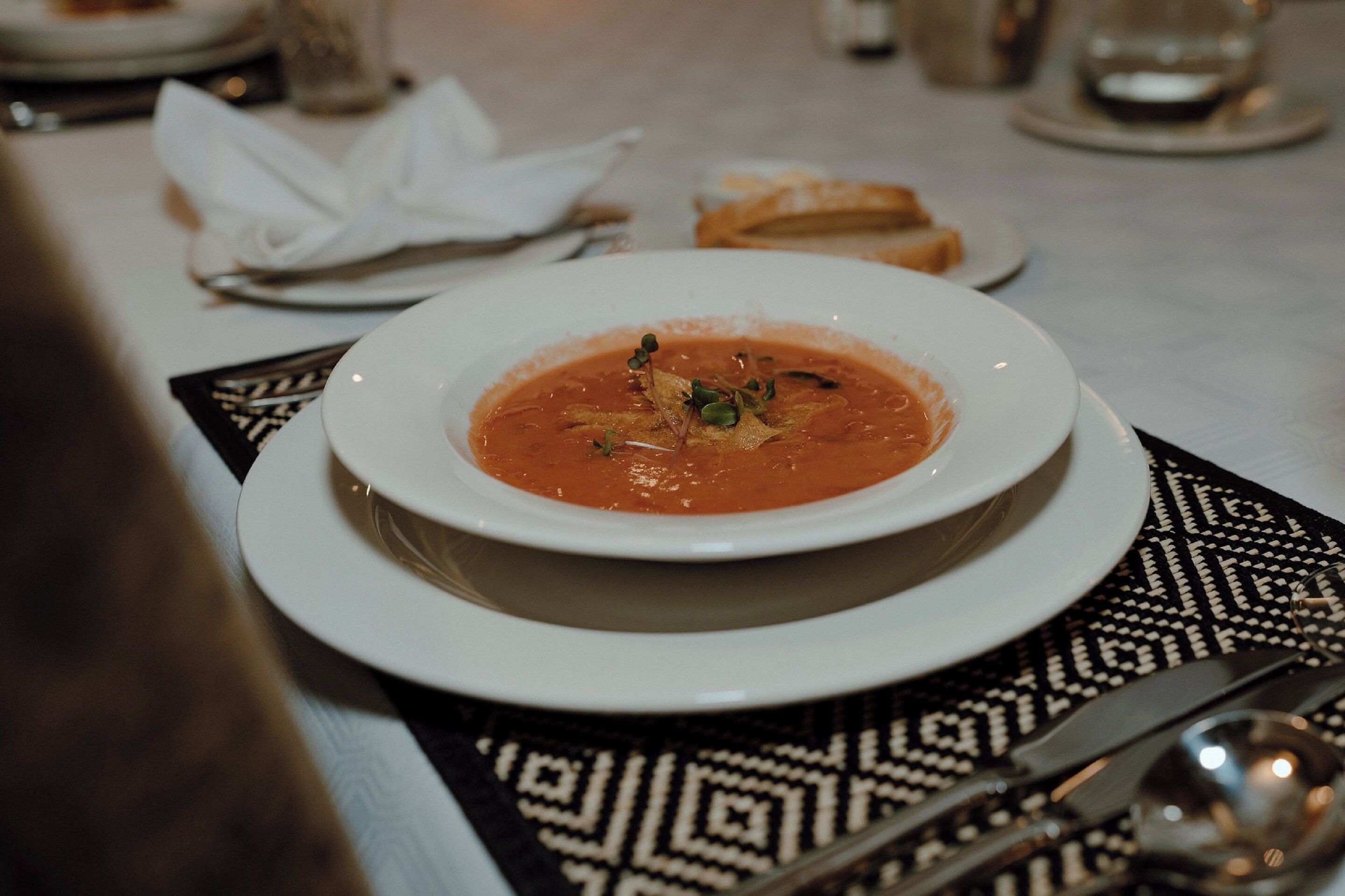Un bol de soupe sur une assiette blanche, posé sur un set de table à motifs.