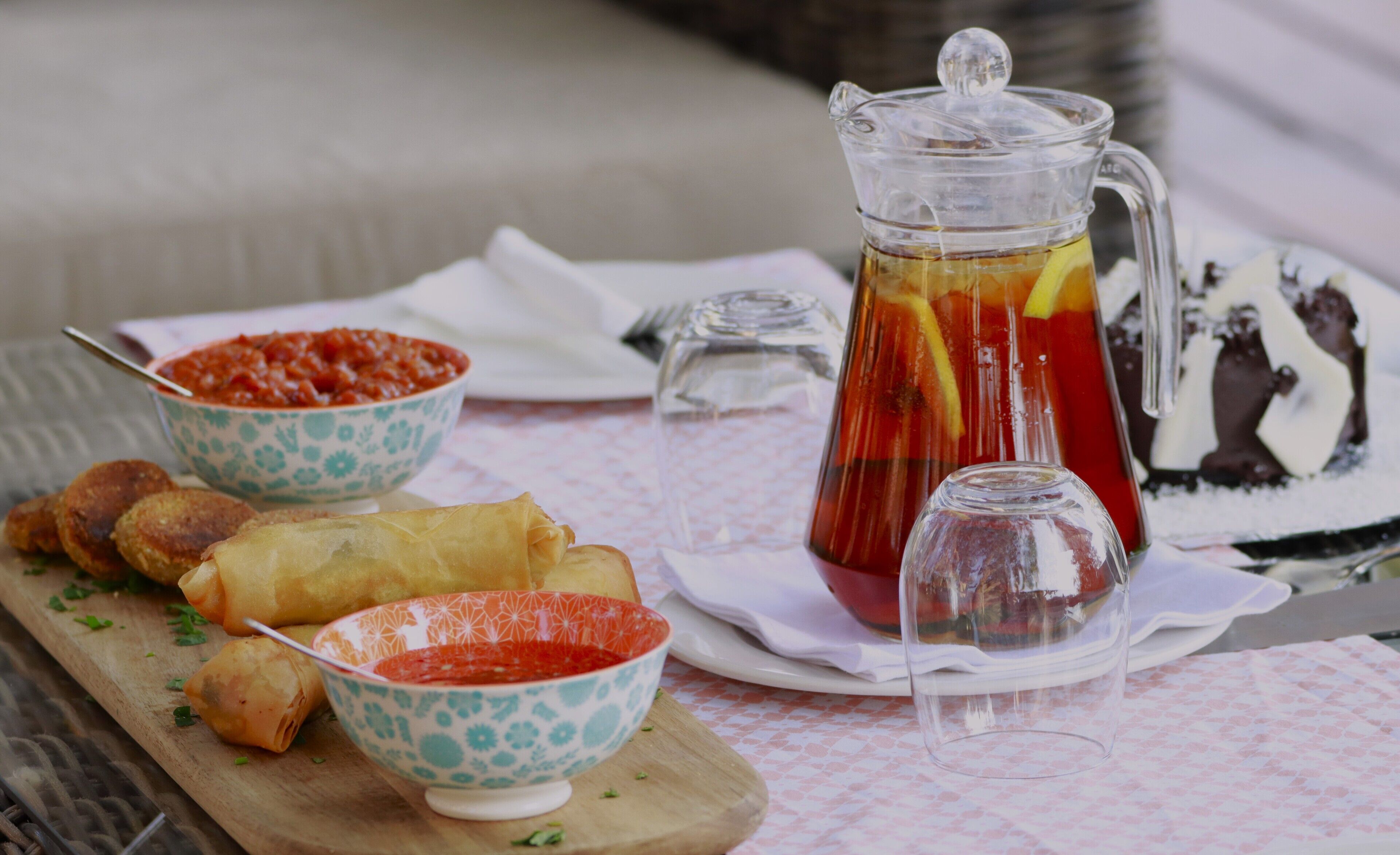 Una mesa con comida, incluyendo una jarra de té helado, un tazón de salsa de tomate y rollitos primavera.