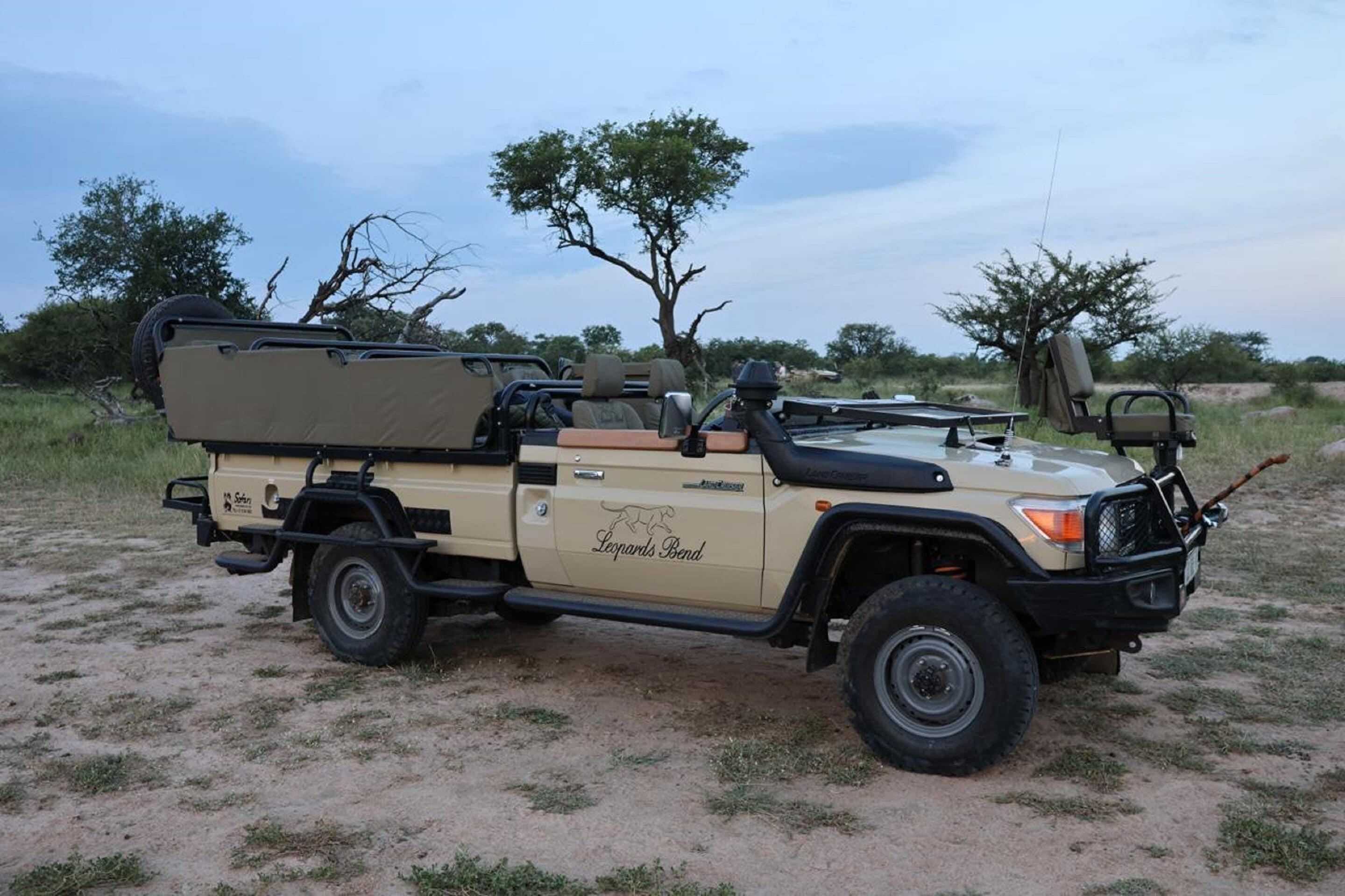 A beige safari vehicle with a roof tent and a spare tire mounted on the back.
