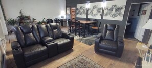 A living room with a black leather sofa, a dining table with chairs, and a rug. - Spacious lodge with custom bunk rooms in prime Lake Area with ample parking. (Waubay)