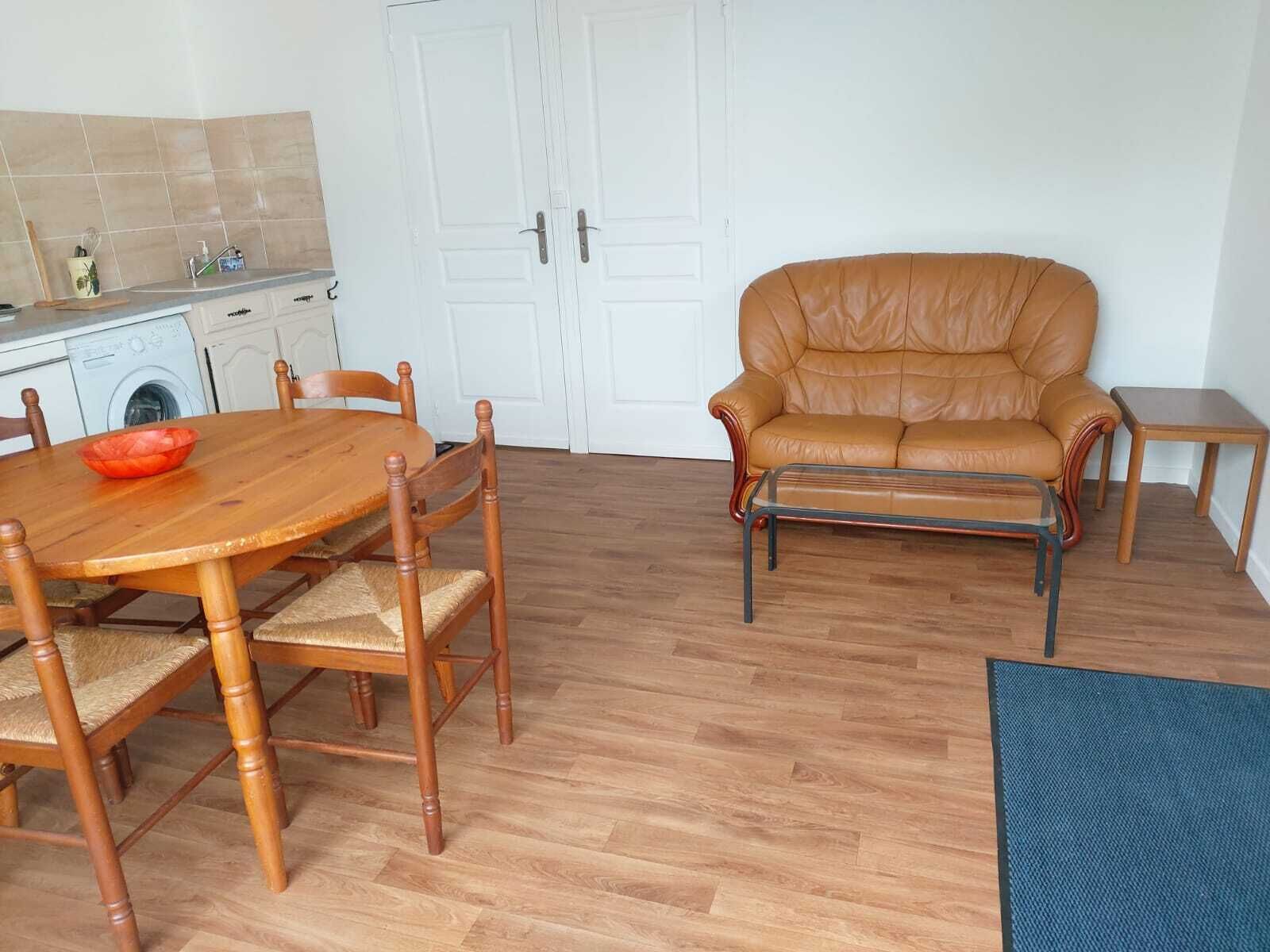 Een kamer met een houten eettafel en stoelen, een leren bank, een klein bijzettafeltje en een wasmachine op de achtergrond.