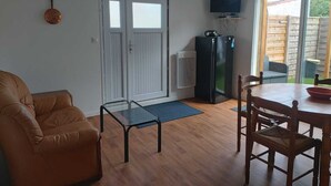 A compact living space with a sofa, a glass-top table, a dining table with chairs, a black refrigerator, and a TV mounted on the wall. - Maison de Vacances Pour 2 Personnes. Animal Accepté - Plage-mer 10 min (Grues)