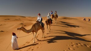 A desert landscape with people riding camels. - Golden Desert Camp (Bidiya)