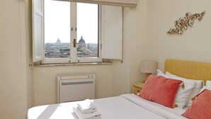 Quarto de hotel com uma cama, janela com vista para a paisagem urbana, radiador e abajur.