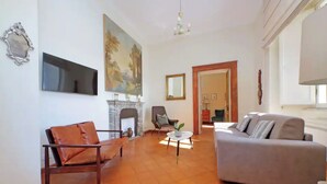 Uma sala de estar com lareira, um sofá, uma poltrona e uma televisão na parede.