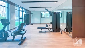 A gym with cardio machines, weightlifting equipment, and large windows offering views of the city. - Luxurious 1-br Apt With Balcony in Azizi Fawad (Dubai)