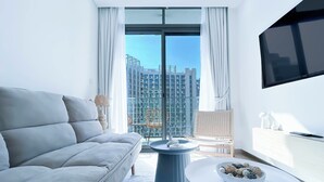 A modern living room with a grey sofa, a round coffee table, and a TV mounted on the wall. - Luxurious 1-br Apt With Balcony in Azizi Fawad (Dubai)