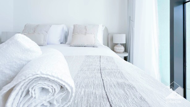 A neatly made bed with white linens, a bedside lamp, and a view of a window with curtains. - Luxurious 1-br Apt With Balcony in Azizi Fawad (Dubai)