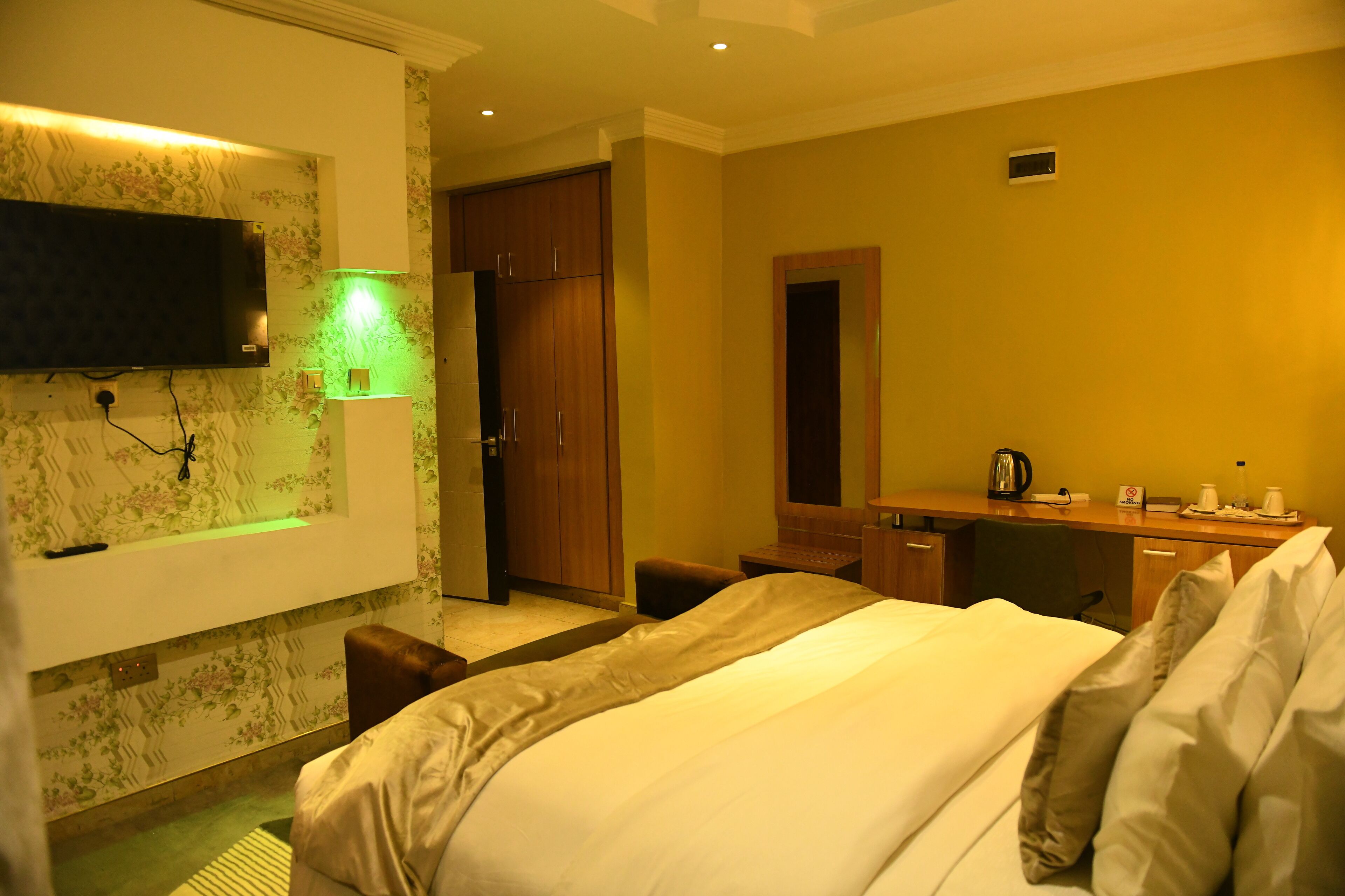 A hotel room with a bed, a desk, a mirror, a TV, and a bathroom with a shower and toilet.