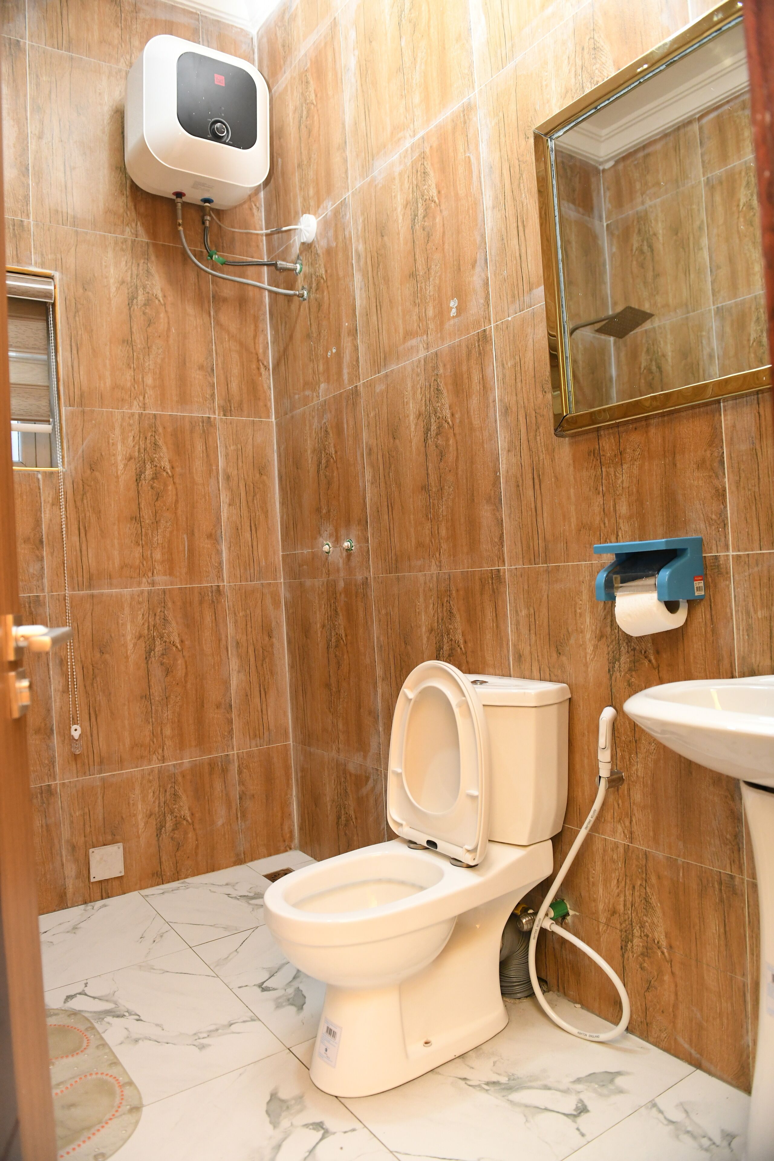 A bathroom with a toilet, a hand dryer, a paper towel dispenser, and a sink.