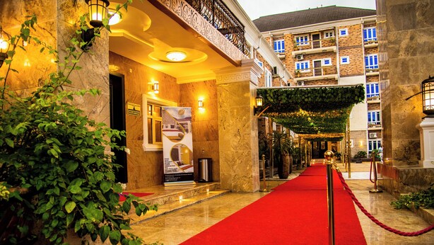 A hotel entrance with a red carpet, reception desk, and a sign indicating the reception area. - Portland Resort Hotel (Port Harcourt)