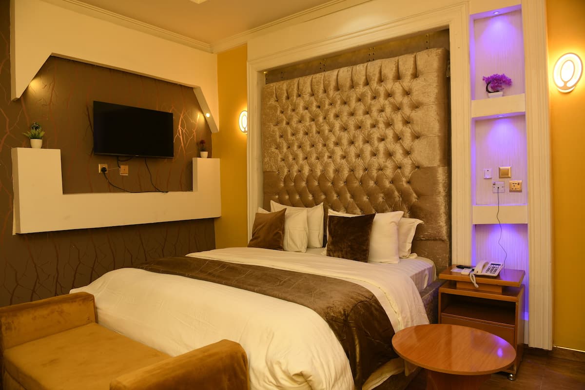 Ein Hotelzimmer mit einem großen Bett, einem an der Wand montierten Fernseher, einem Nachttisch mit Lampe und einem kleinen runden Tisch.