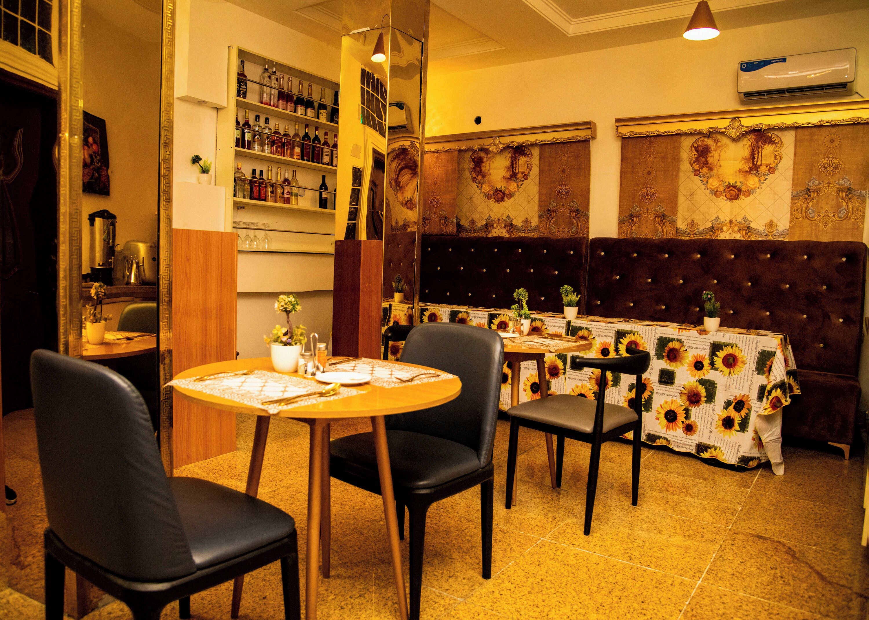 Un restaurante con una mesa redonda preparada para cuatro, cabinas tapizadas oscuras y una pared llena de botellas de vino.