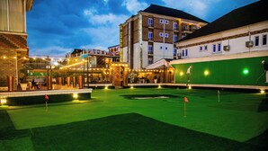A golf course with a green field, a putting green, and a building with a balcony. - Portland Resort Hotel (Port Harcourt)