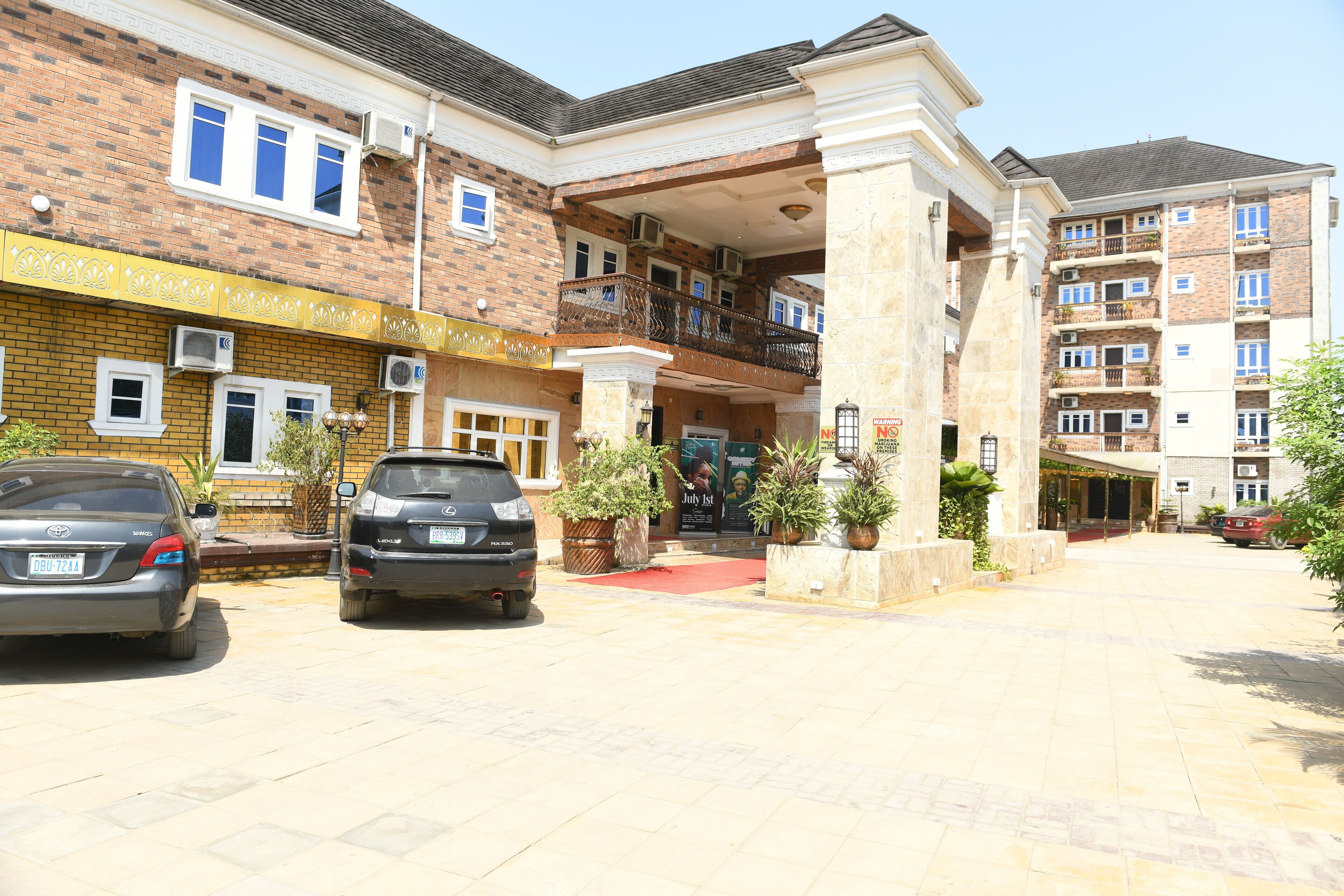 A building with a brick facade, a covered entrance, and a red carpet leading to the entrance. There are two cars parked in front.