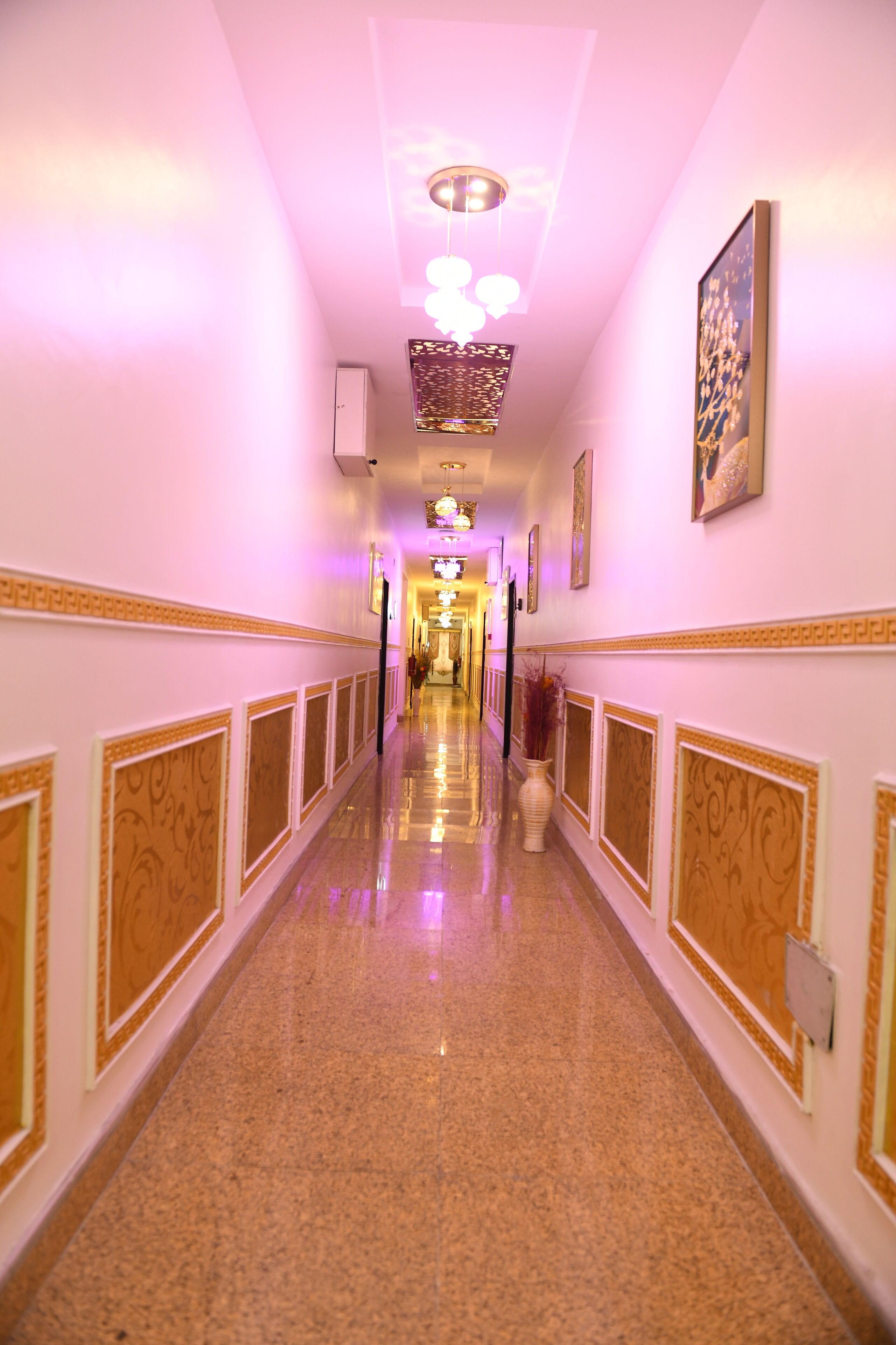 A long, narrow hallway with ornate wall panels and a polished floor, leading to a brightly lit room at the end.
