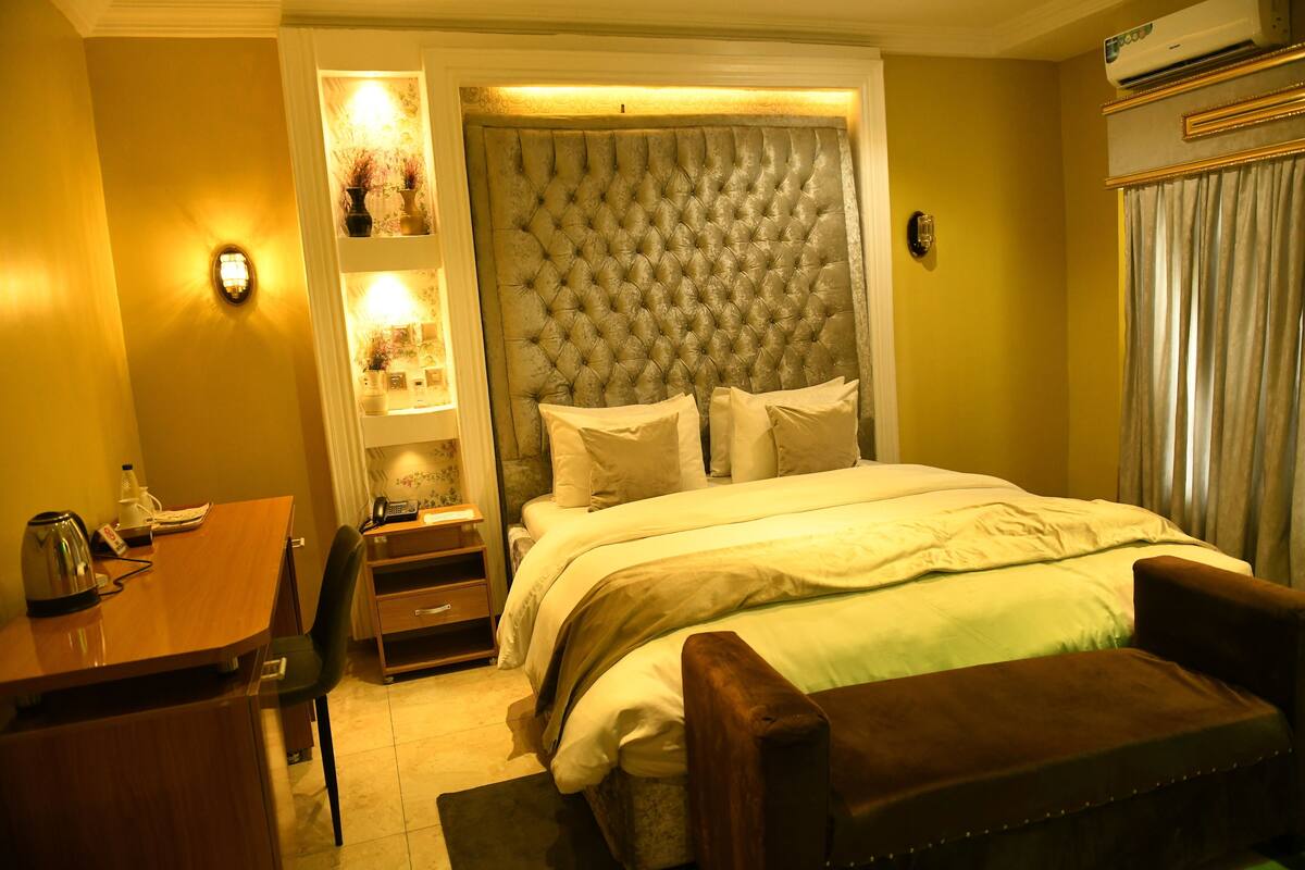 Ein Hotelzimmer mit einem großen Bett, einem Schreibtisch mit Stuhl, einem kleinen Tisch und einer Bank.