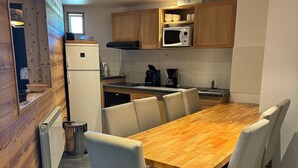A compact kitchen with wooden cabinets, a built-in microwave, a coffee maker, and a dining table with chairs.