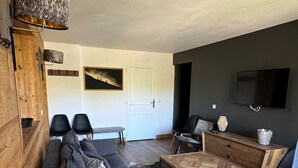 A modern living room with a dark accent wall, a wooden cabinet, a sofa, a coffee table, and a TV mounted on the wall.