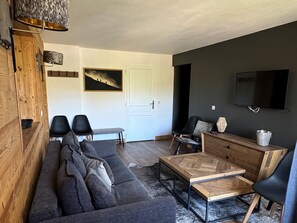 Una sala de estar moderna con una pared de acento oscura, un mueble de madera, un sofá, una mesa de centro y un televisor montado en la pared.