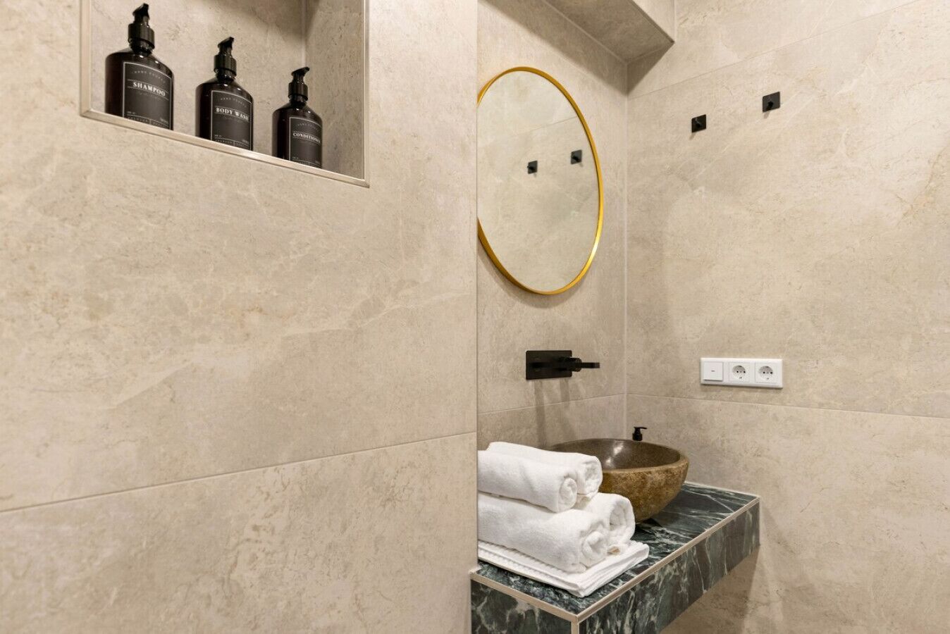 Une salle de bain avec un lavabo en marbre, un grand miroir et trois bouteilles de shampoing et d’après-shampoing.
