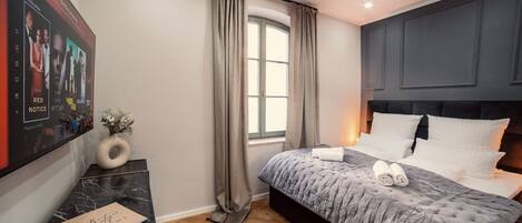 Una habitación de hotel moderna con una cama grande, una mesita de noche de mármol, un cuadro enmarcado en la pared y una ventana con cortinas.