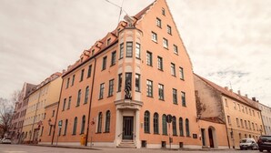 A large, historic building with a prominent corner entrance, multiple windows, and a statue in front. - NEW LUXUS Suite | TWO Kingbeds | Netflix | Center (Augsburg)