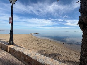 A beach with a stone wall, a lamp post, and a clear sky.
