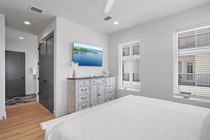 Ein Schlafzimmer mit Bett, Kommode, Fernseher an der Wand und einem Fenster mit Jalousien.