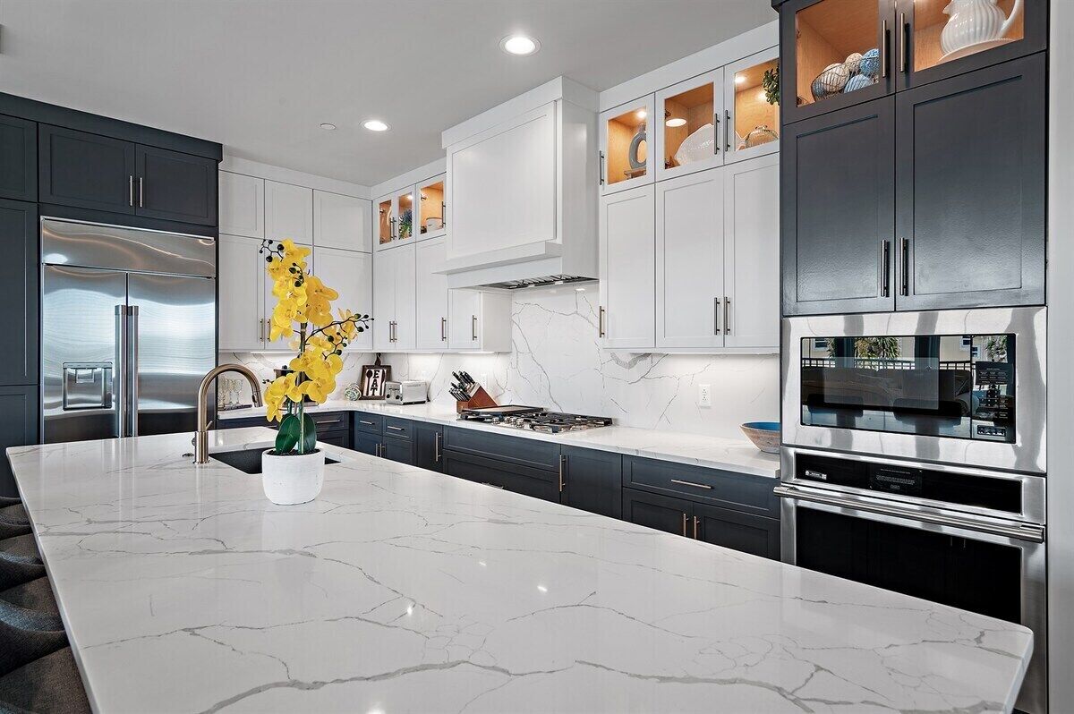 A modern kitchen with a marble island, stainless steel appliances, and a variety of cabinets.