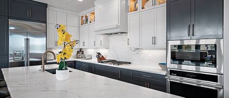 A modern kitchen with a marble island, stainless steel appliances, and a variety of cabinets.