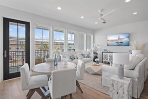 A modern living room with a round dining table, white sofas, and a large window with a view of the city.