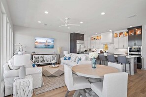 Ein modernes Wohnzimmer mit einem weißen Sofa, einem runden Couchtisch und einem Essbereich mit Stühlen.