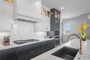 A modern kitchen with white marble countertops, dark cabinetry, and stainless steel appliances.