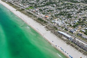An aerial view of a coastal area with a beach, residential buildings, and a road.