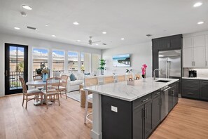 Una cocina moderna con una isla grande, armarios oscuros y un comedor con sillas de mimbre.