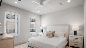 Ein Schlafzimmer mit einem Bett, Nachttischen, einem Deckenventilator und Fenstern mit Jalousien.