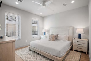 A bedroom with a bed, bedside tables, a ceiling fan, and windows with blinds.