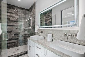 A modern bathroom with a glass shower enclosure, two sinks, and a large mirror.