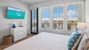 Ein Schlafzimmer mit einem Bett, einem Schminktisch, einem an der Wand montierten Fernseher und einem Fenster mit Jalousien.