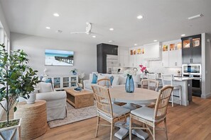 Una cocina moderna con armarios blancos, horno integrado y comedor con sillas de mimbre y una mesa redonda.