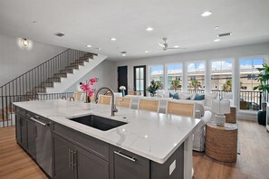 A modern kitchen with a large island, dark cabinetry, and a staircase leading to an upper level.
