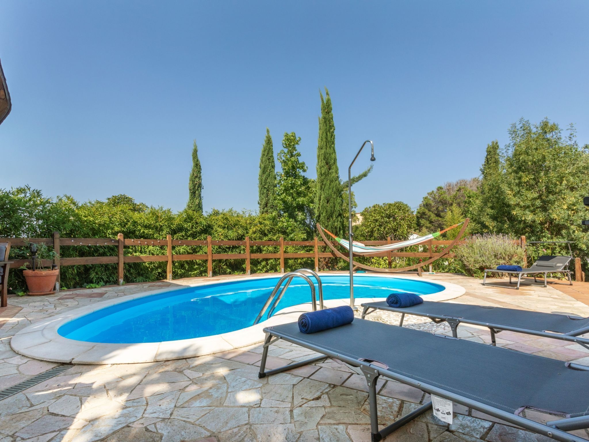 Una piscina con cerco de madera, sillas de descanso y una hamaca.