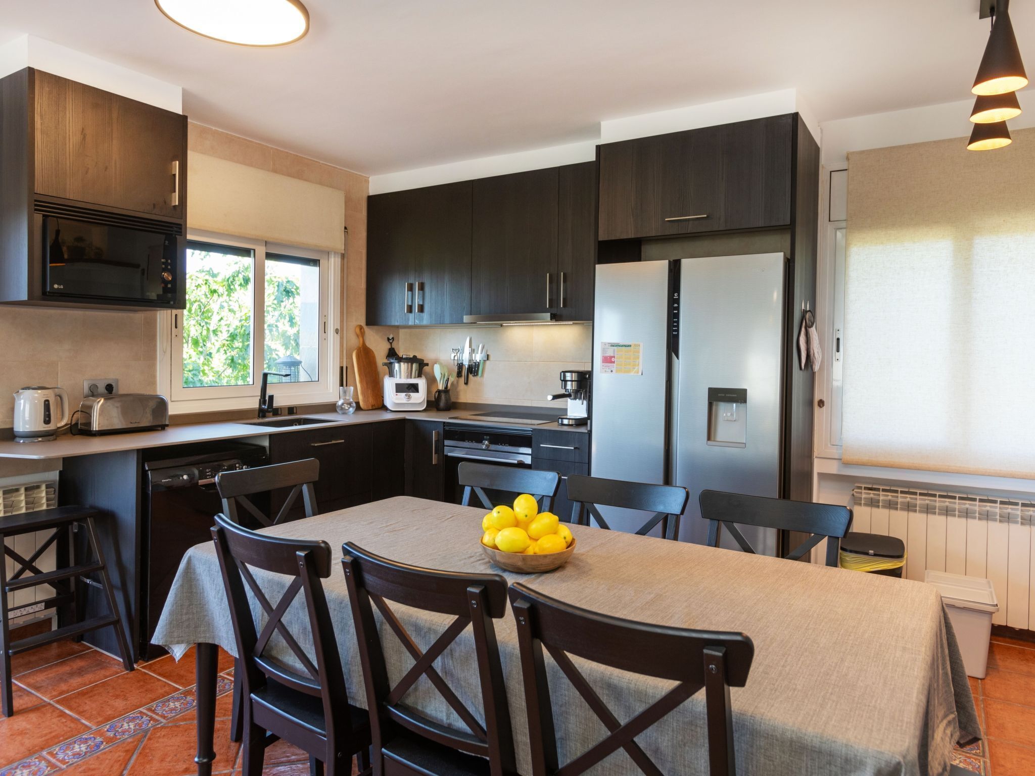 Una cocina moderna con armarios oscuros, un refrigerador de acero inoxidable y una mesa de comedor con sillas.