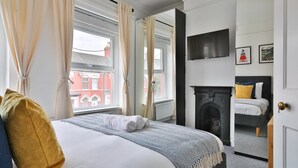 A hotel room with a bed, a fireplace, a TV mounted on the wall, and a view of the outside. - Stunning 2 Bedroom Cardiff Bay House (Cardiff)