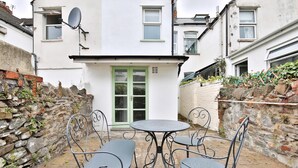 A courtyard with a round table and four chairs, a white building with a green door, and a stone wall. - Stunning 2 Bedroom Cardiff Bay House (Cardiff)