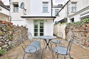 A courtyard with a round table and four chairs, a white building with a green door, and a stone wall. - Stunning 2 Bedroom Cardiff Bay House (Cardiff)