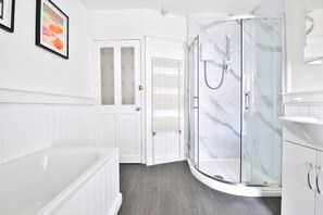 A modern bathroom with a glass shower enclosure, a white bathtub, and a door leading to another room. - Stunning 2 Bedroom Cardiff Bay House (Cardiff)