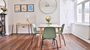 A dining area with a table, chairs, a vase with flowers, a mirror, and framed artwork on the wall. - Stunning 2 Bedroom Cardiff Bay House (Cardiff)