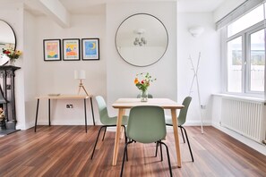 A dining area with a table, chairs, a vase with flowers, a mirror, and framed artwork on the wall. - Stunning 2 Bedroom Cardiff Bay House (Cardiff)